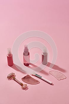 Rose quartz facial massage tools such as gua sha stone scrapers, face roller and beauty products in plastic bottles