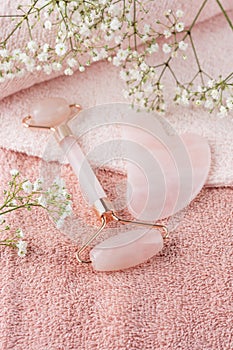 Rose quartz facial roller and guasha stone for anti-aging skin care massage on pink towel