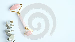 Rose quartz jade roller and eucalyptus leaf on blue background. Facial massage roller, anti-aging, anti-wrinkle beauty skincare