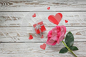 Rose with red paper hearts and gift box on white wooden background. Love symbol concept.