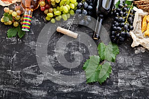 Rose red wine in bottles cheese, white pink and black grapes with vine plant on dark concrete background. Assortment