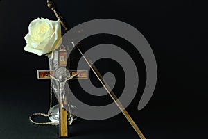 Rose in tin cup, dagger-stylet and crucifix with inlay and gilded chain souvenirs from Germany on black background. Symbolic