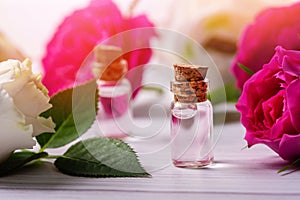 Rose water or essential oil in glass bottles with flowers on wooden table