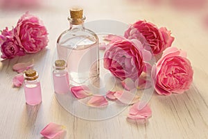 Rose water or oil bottles on wooden white background. Beautiful pink flowers and petals, aromatherapy and SPA concept
