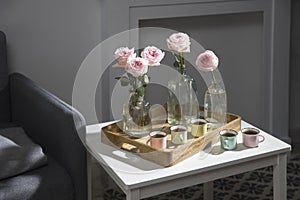 Rose White Pink O`hara. Pink roses in three different shaped bottles on a tray with five small espresso cups on the coffee table