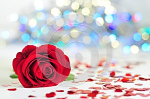 Rose on the white tablecloth between hearts, colorful lights in the background