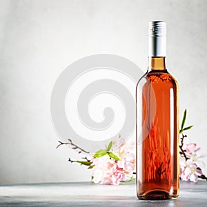 Rose wine bottle on the gray table and spring pink flowers. Rosado, rosato or blush wine tasting in wineshop, bar concept. Copy