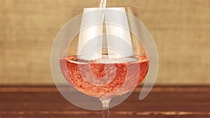 Rose wine pouring into glass on wooden table