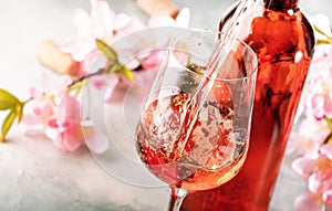 Rose wine pouring out of the bottle, gray bakcground, pink flowers. Rosado, rosato or blush wine tasting in wineshop, bar concept