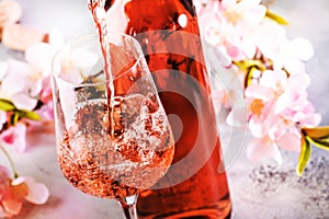 Rose wine pouring out of the bottle, gray bakcground, pink flowers. Rosado, rosato or blush wine tasting in wineshop, bar concept