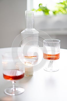 Rose wine in trendy ribbed wineglasses and decanter on white table