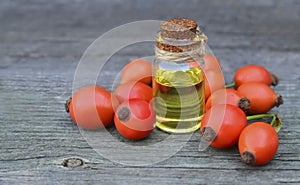 Rosehip essential oil in a glass bottle with rose hips berries on old wooden table for skin care or spa.