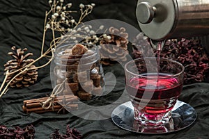 Roselle tea Jamaica sorrel, Rozelle or hibiscus sabdariffa  is poured from a kettle into glass cup  with dry roselle and brown