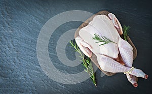 Rosemary chicken meat wooden cutting board / fresh raw chicken whole on black plate background