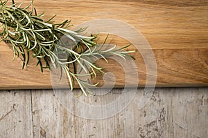 Rosemary on a chopping board lying on top of an aged wooden sur