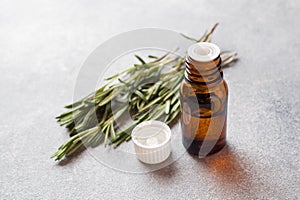 Rosemary essential oil in a glass bottle with fresh branch rosemary herb on grey table for spa,aromatherapy and bodycare.Copy