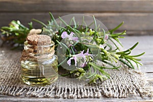 Rosemary essential oil in a glass bottle with fresh green rosemary herb on old wooden table for spa, aromatherapy and bodycare.