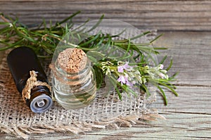 Rosemary essential oil in a glass dropper bottle with fresh green rosemary herb on old wooden table for spa,aromatherapy and body