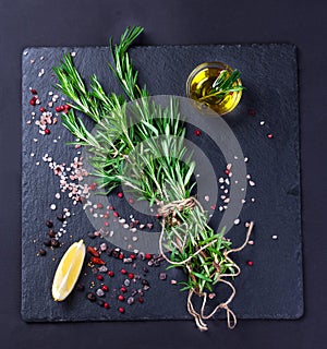 Rosemary plant, salt and spices on black slate board