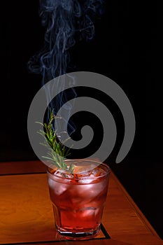 Rosemary smoked negroni cocktail. Negroni cocktail glass on wooden table with branch of smoking rosemary