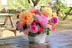 Roses, asters, dahilia in the apple garden on a wooden table. Floristic design. Flowers in sunny day. Country life.