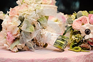 Roses bouquet wrapped in ribbon in front of wedding cake.