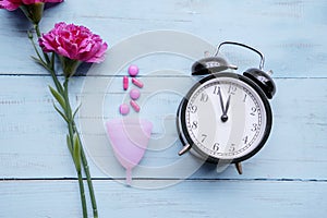 Roses, pills and sanitary cup with alarm clock