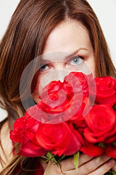 These roses smell great. Portrait of an attractive young woman peering over a bouquet of roses.