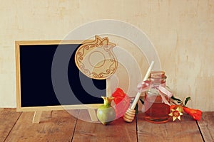 Rosh hashanah (jewesh holiday) concept - blackboard, honey and pomegranate over wooden table. traditional holiday symbols.