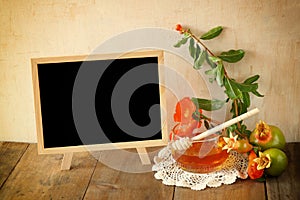 Rosh hashanah (jewesh holiday) concept - blackboard, honey and pomegranate over wooden table. traditional holiday symbols.