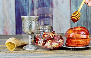 rosh hashanah jewesh holiday concept - shofar, torah book, honey, apple and pomegranate over wooden table. a kippah a yamolka
