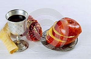 rosh hashanah jewesh holiday concept - shofar, torah book, honey, apple and pomegranate over wooden table. a kippah a yamolka