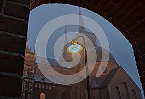 Roskilde cathedral illuminated by a street lamp in the fog under an arch