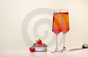 Rossini summer alcoholic cocktail drink with sparkling wine or prosecco, strawberry puree and ice in champagne glasses. Beige pink