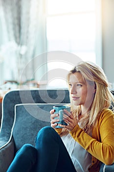 The rosy glow of recollection. a young woman relaxing on her sofa with a cup of coffee.