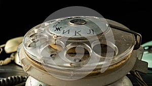 Rotary dialer of an old dirty telephone with round holes and numbers on a black background. Plastic transparent dialing