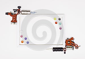 Rotary and induction tattoo machines on a white background, white frame, free space for text, colored tattoo ink in plastic jars.