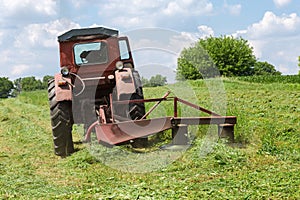 Rotary mower on small old tractor during operation on hayfield