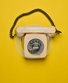 A rotary retro phone on a yellow background.