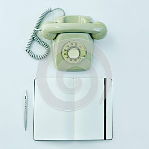 Rotary telephone, pen and blank notepad on a table