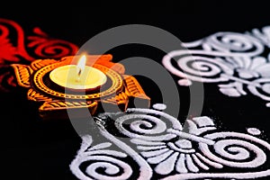 Rotated view of beautiful shining terracotta lamp and red white rangoli design on black background. diwali concept
