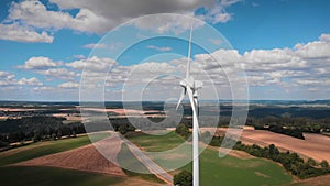 Rotating blades of wind turbine at wind farm against blue sky and fluffy clouds. Green and renewable energy concept. Renewable ene