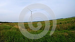 Rotating blades of a windmill propeller in field on blue sky background. Wind power generation. Pure green energy.