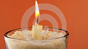 Rotating Burning Candle with a Bright Flame on an Isolated Orange Background. 4K