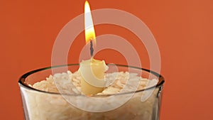 Rotating Burning Candle with a Bright Flame on an Isolated Orange Background. 4K
