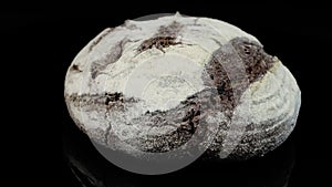 Rotating fresh black bread sprinkled with flour on a dark background.