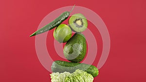 rotating fresh green vegetables and fruits on a red background. Creative food concept. Equilibrium floating food balance