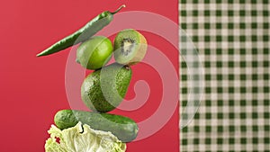 rotating fresh green vegetables and fruits on a red background. Creative food concept. Equilibrium floating food balance