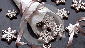 Rotating gingerbread cookies snowflakes in a paper cone on slate table