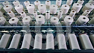 Rotating machines work at a textile factory, spinning clews with white thread.